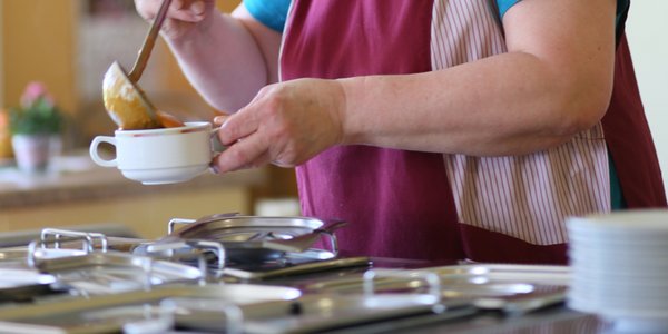 Eine Mitarbeiterin füllt Suppe in Tassen für die Bewohner. 