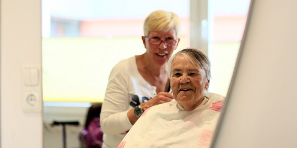 Die Friseurin schneidet die Haare einer Bewohnerin.