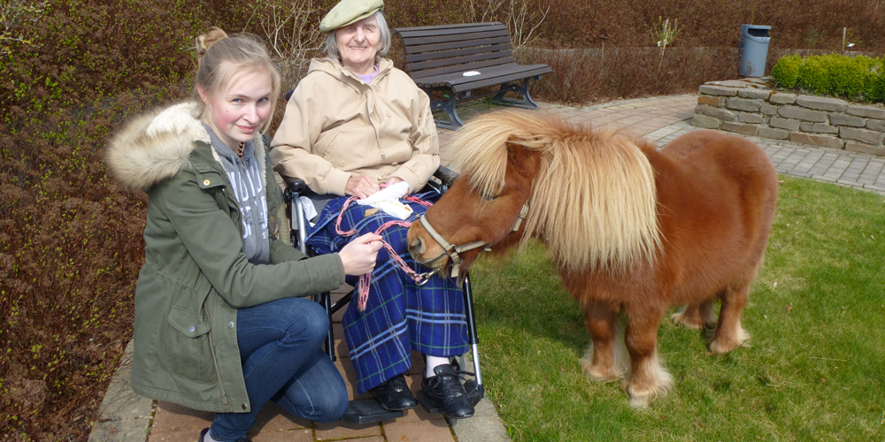Eine Bewohnerin genießt die Zeit beim Pony im Garten.